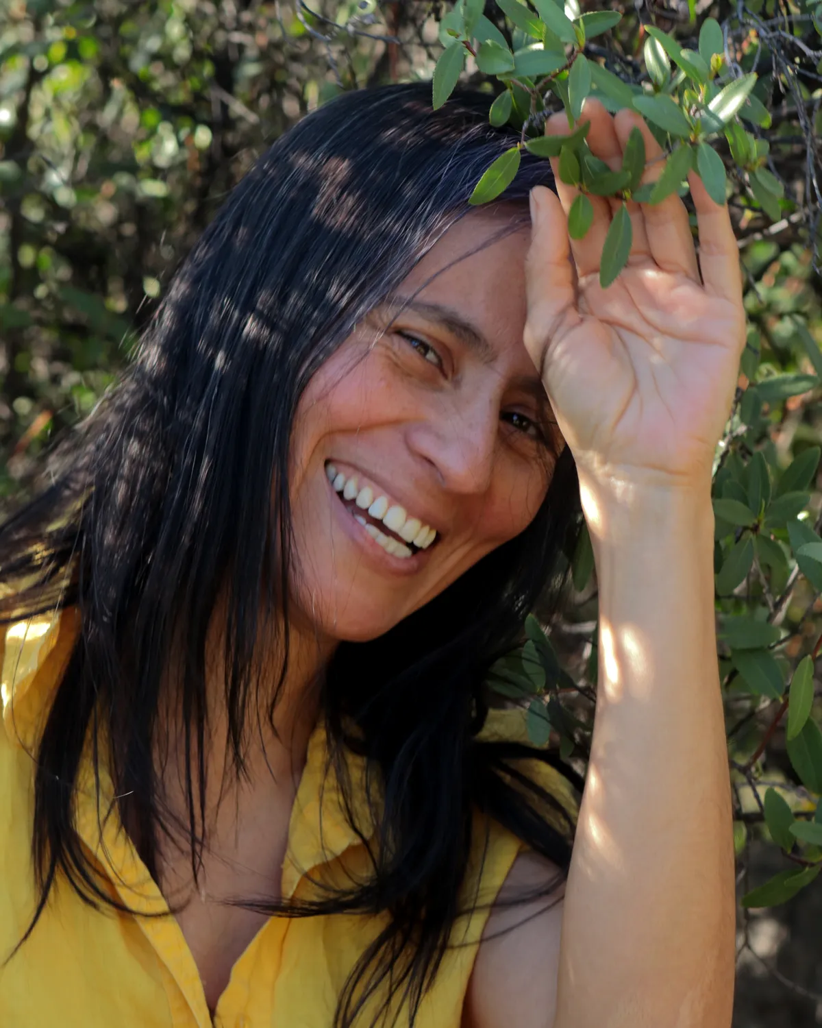 Pamela Gutiérrez sonriendo entre vegetación nativa, sosteniendo una rama