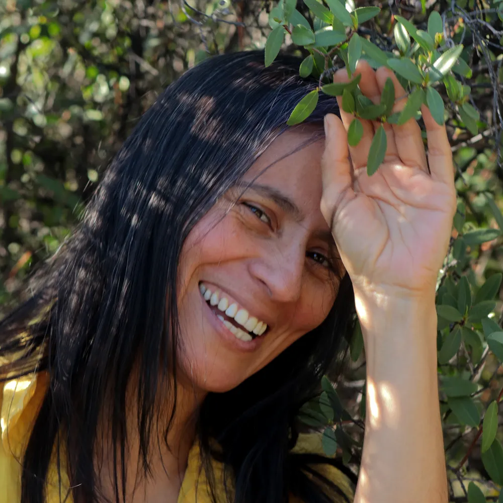 Pamela Gutiérrez sonriendo entre vegetación nativa, sosteniendo una rama